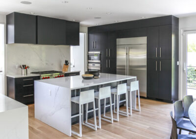 Modern kitchen with dark blue cabinets, marble countertops, stainless steel appliances, and an island with white bar stools